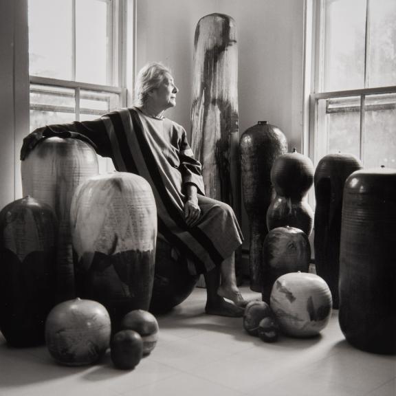 Artist Toshiko Takaezu sits among her works of pottery and looks out the window.